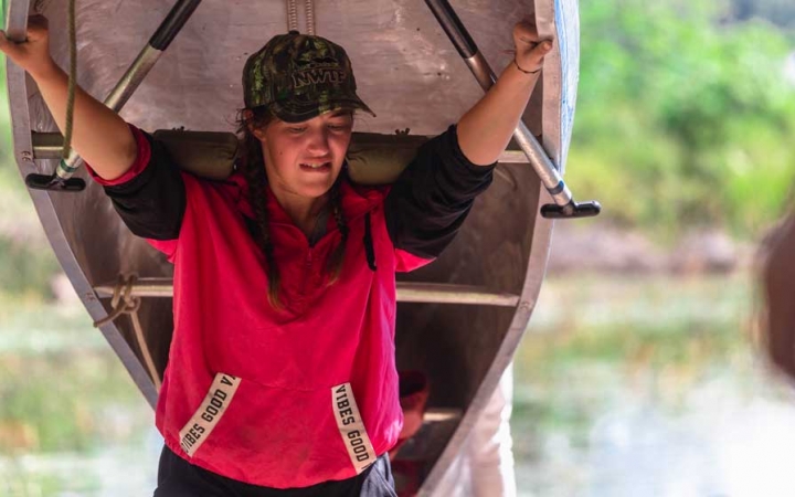 a young person portages a canoe on their shoulders on an outward bound course